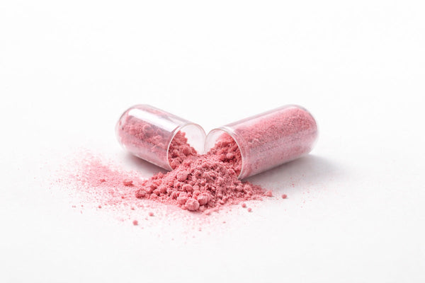 Open clear capsule spilling pink powder onto a white surface.